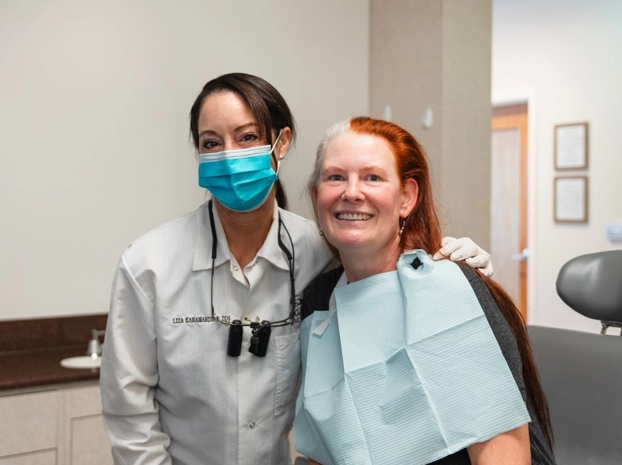 Dentist wearing a mask and a patient with dentures both smiling at the camera.